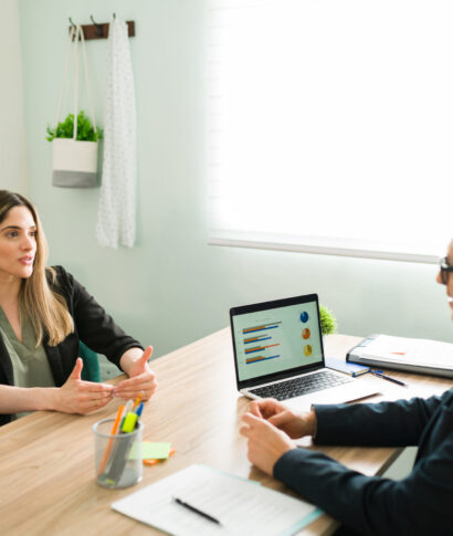 Beautiful coworker talking about work with her latin boss Attractive business professional talking about a work deal and analytic report with her male boss. Female colleague having a meeting with her coworker at the office
