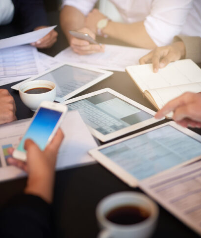Closeup shot of a group of professionals using different devices while sitting together at a table in an office
